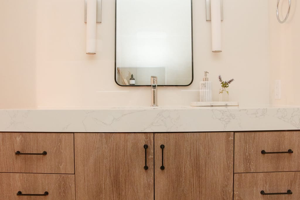 A MCM vanity in a warm basement bathroom with thick quartz top, black hardware