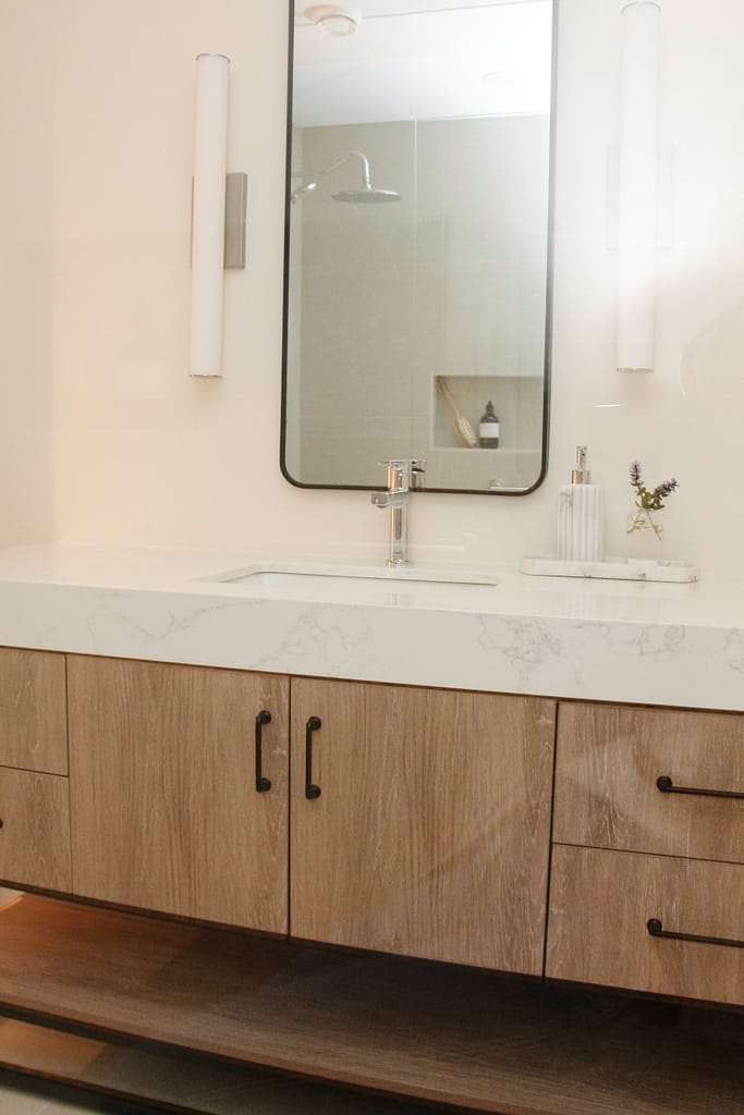 A MCM vanity in a warm basement bathroom with thick quartz top, black hardware, Dove Wing Benjamin Moore