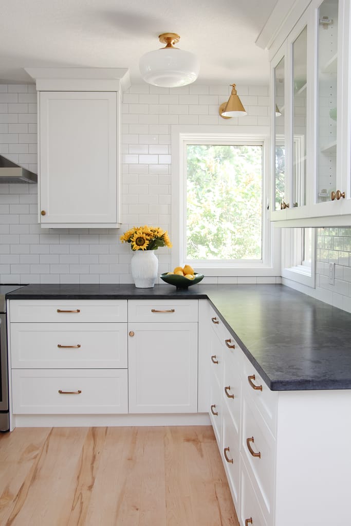 timeless white kitchen cabinets, black quartz counter, gold sconce over window, sunflowers and lemon decor, subway tile to ceiling