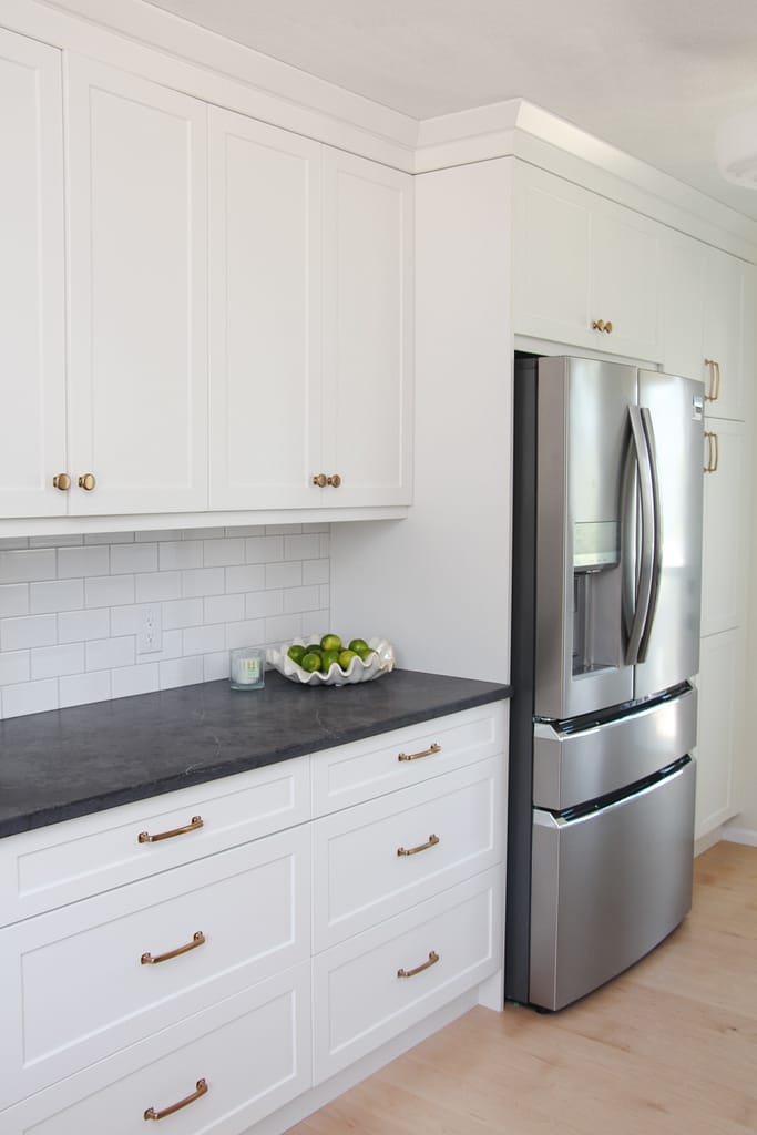 white galley kitchen with black quartz countertop, bowl of limes, gold hardware