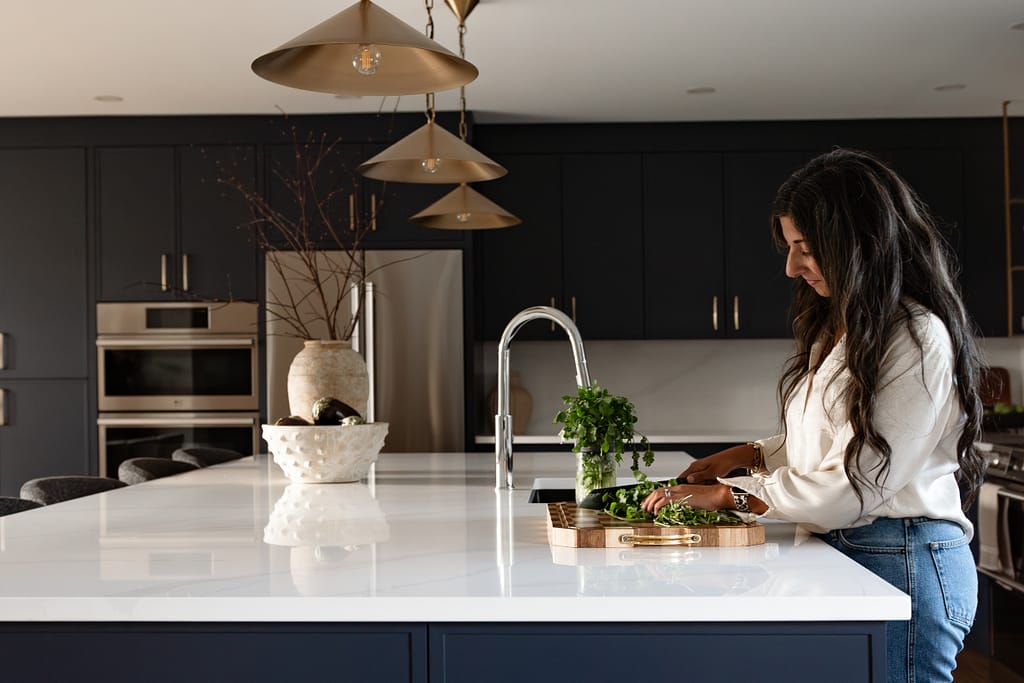 Women in bright renovated kitchen with large island, navy blue cabinetry, and warm wood accents in a family-focused home renovation