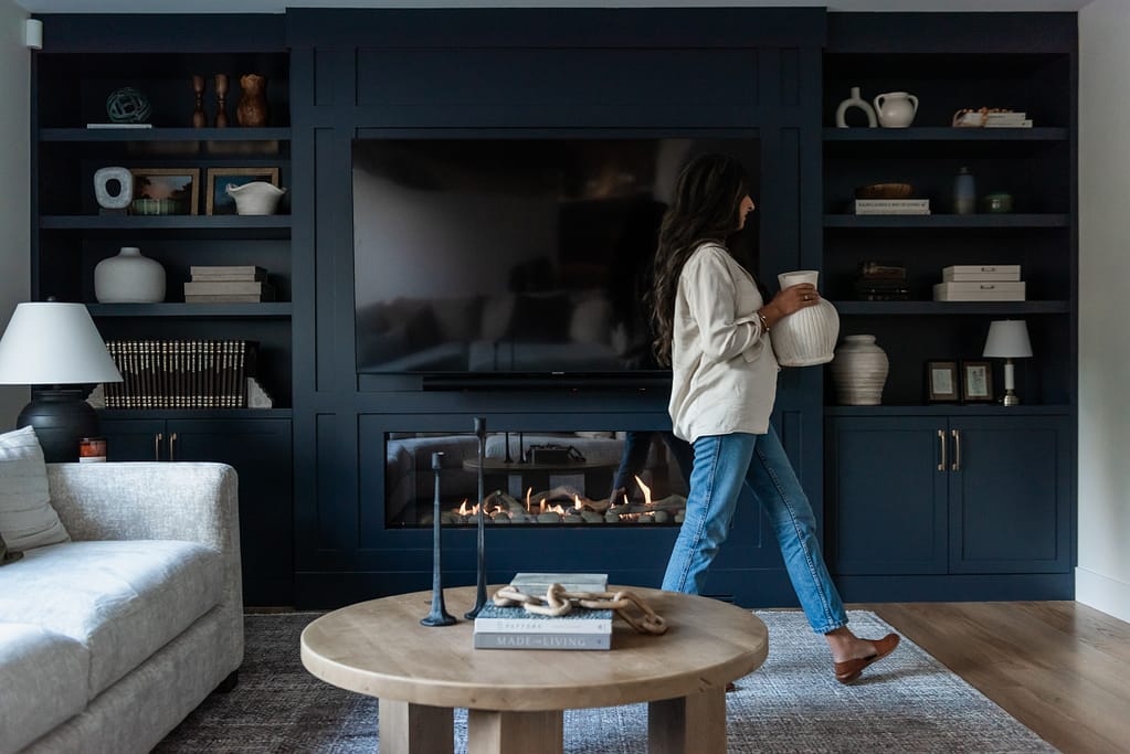 Woman decorating built in cabinetry in modern living room with linear fireplace