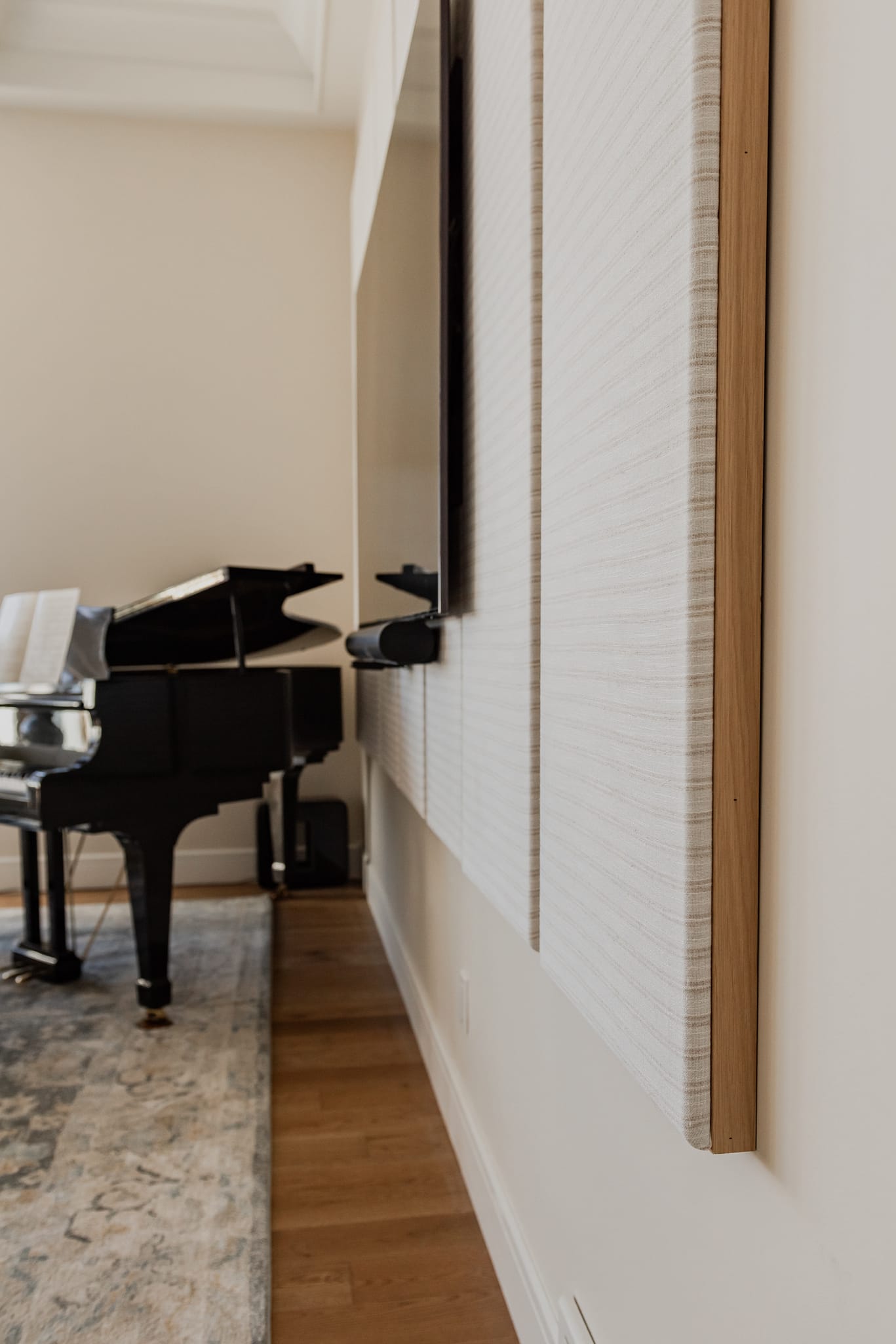 Custom fabric-wrapped acoustic wall panels framed in natural oak, installed behind a television for subtle sound absorption.