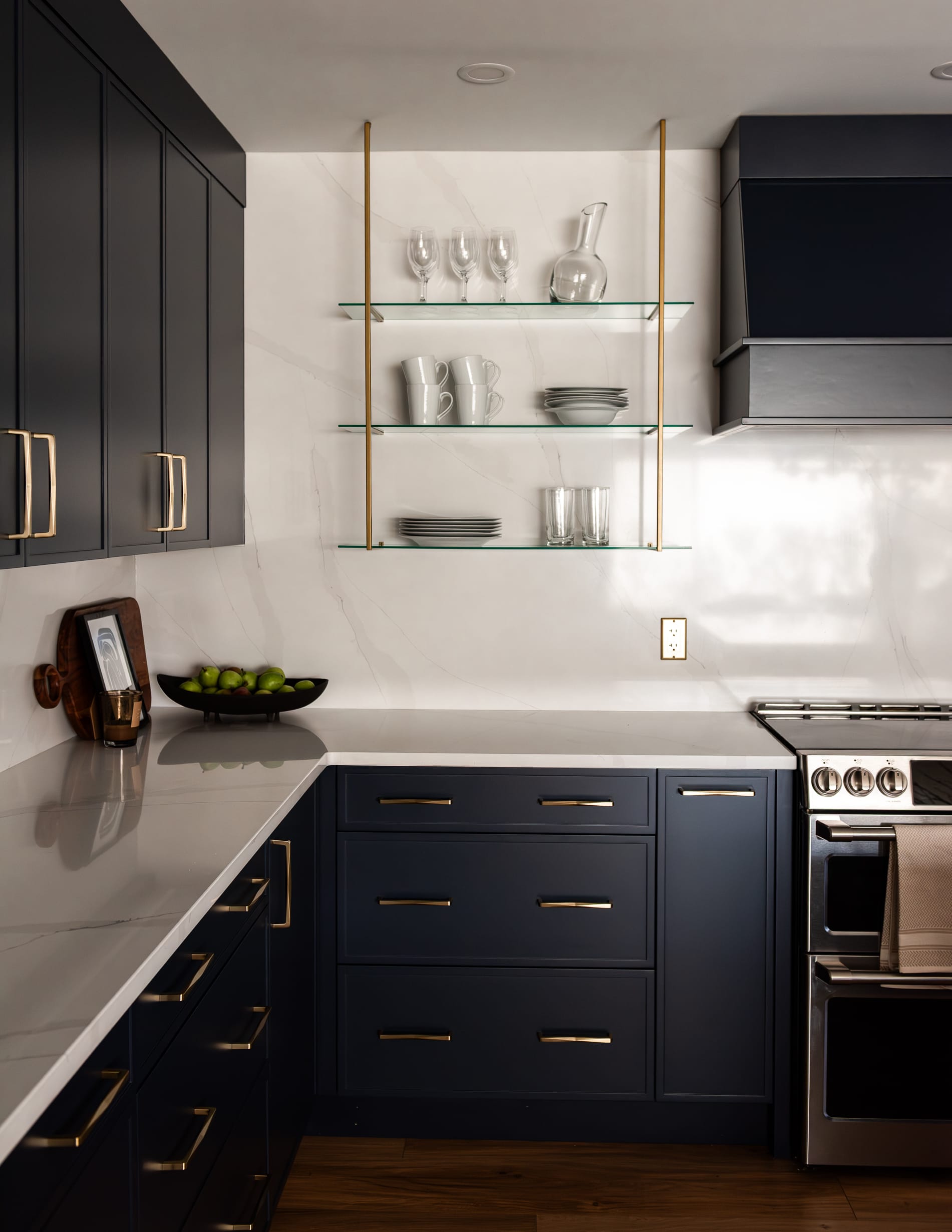 Modern kitchen range wall with navy cabinetry, statement hood, tile backsplash, and wood shelving