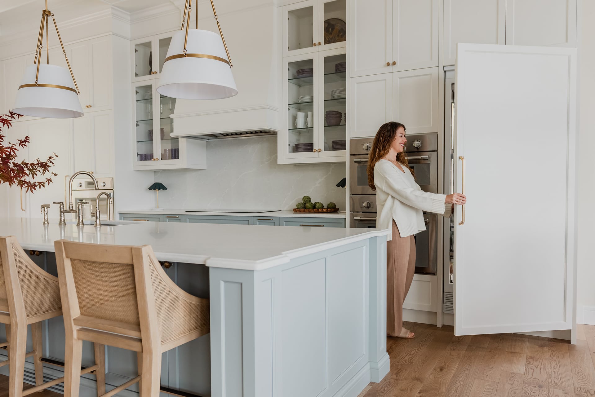 Woman in Custom 6-foot range hood feature wall with integrated Thermador appliances, coffered ceilings, and a spacious entertaining island.