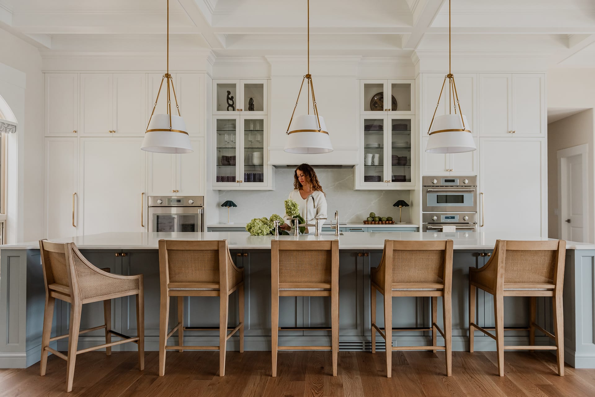 Woman in Custom 6-foot range hood feature wall with integrated Thermador appliances, coffered ceilings, and a spacious entertaining island.