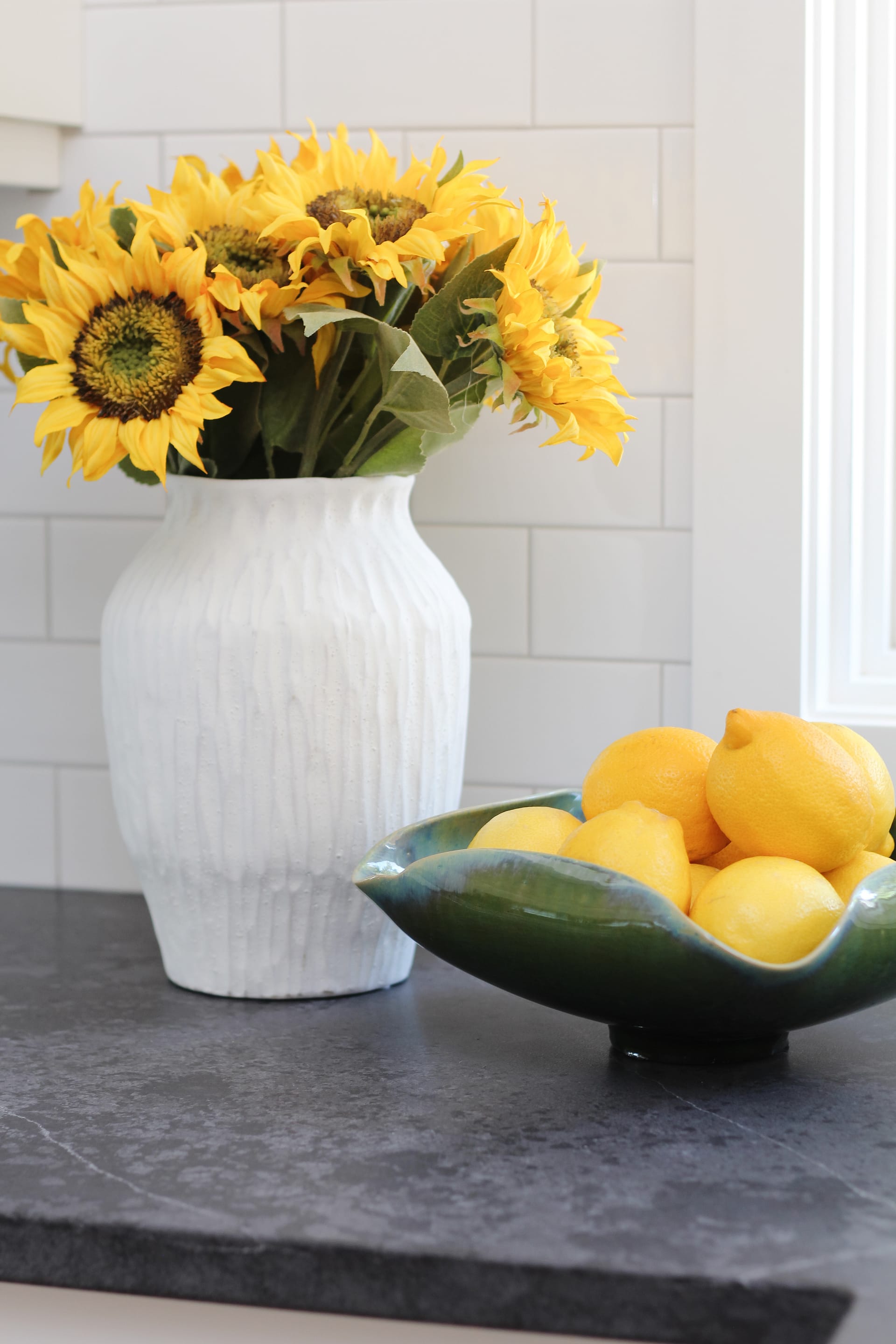 timeless white kitchen cabinets, black quartz counter, sunflowers and lemon decor, subway tile to ceiling