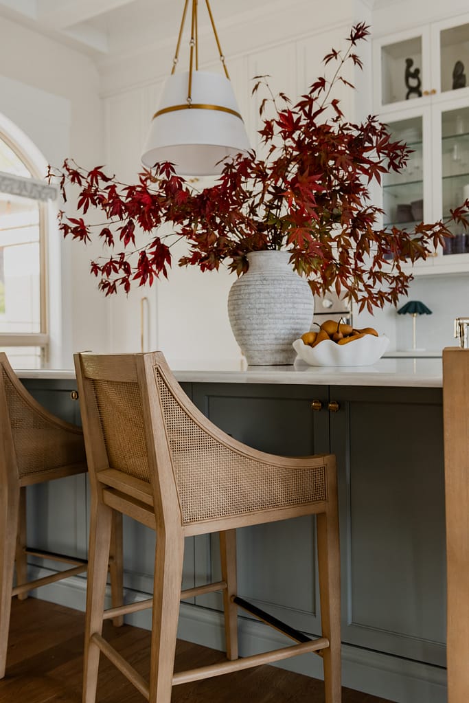 Range hood feature wall with integrated Thermador appliances, coffered ceilings, cane wood bar stools, and a spacious entertaining island