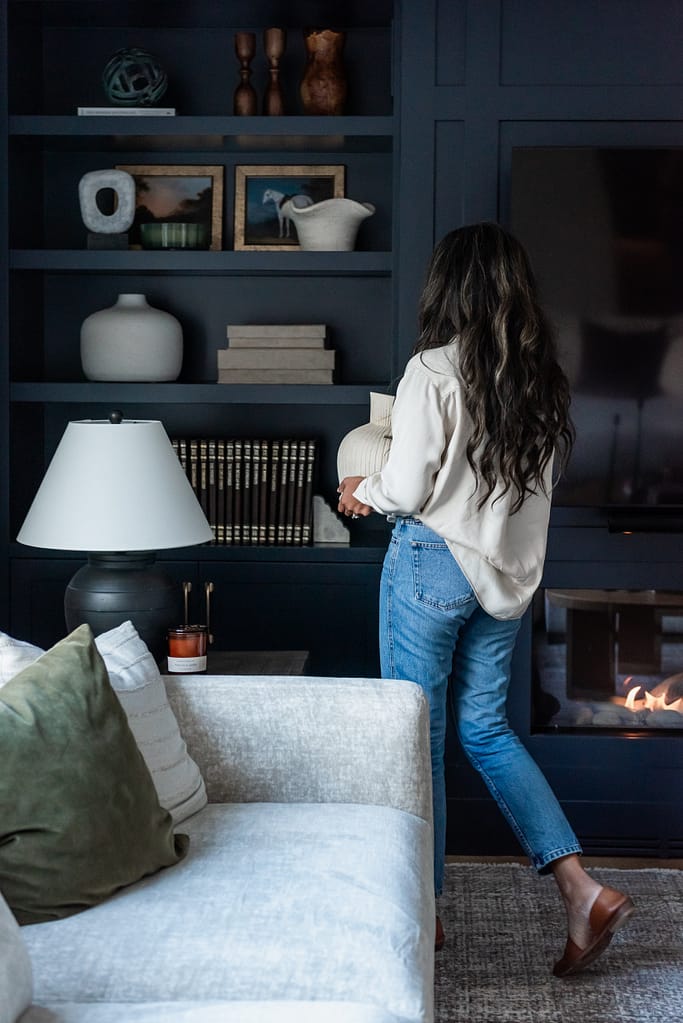 Woman decorating built in cabinetry in modern living room with linear fireplace
