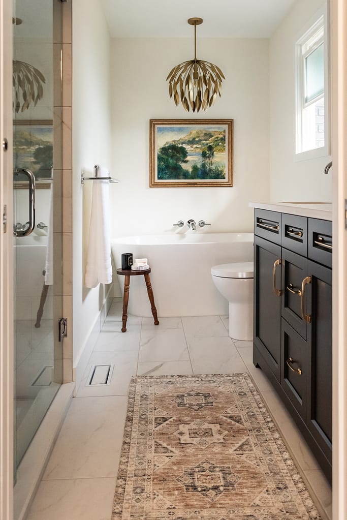 Renovated primary ensuite with deep hunter green vanity, freestanding tub, and brass lighting