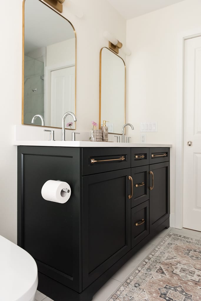 Renovated primary ensuite with deep hunter green vanity, freestanding tub, and brass lighting