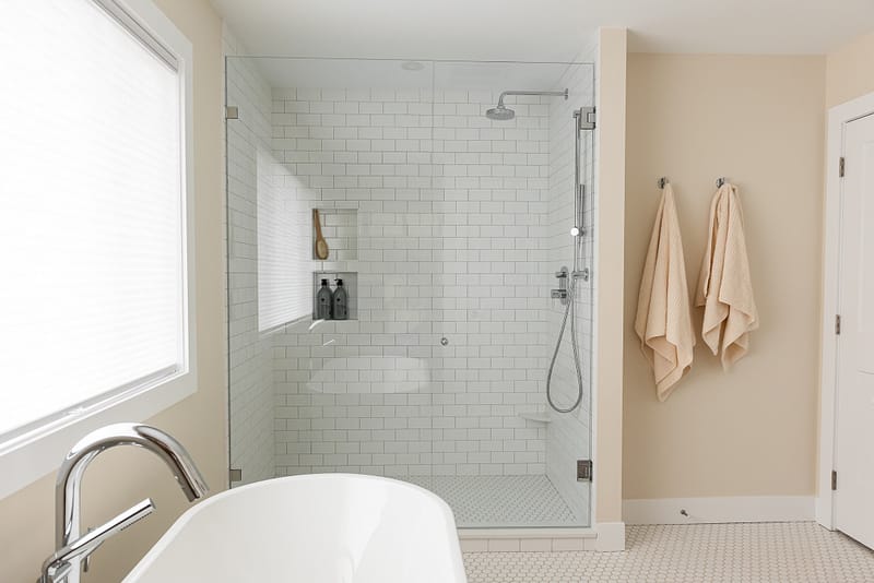 transitional primary ensuite, warm wood tones and white tile, stand alone tub, walk in shower