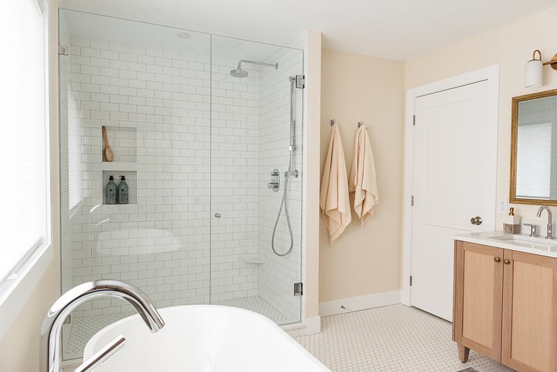 transitional primary ensuite, warm wood tones and white tile, stand alone tub, walk in shower