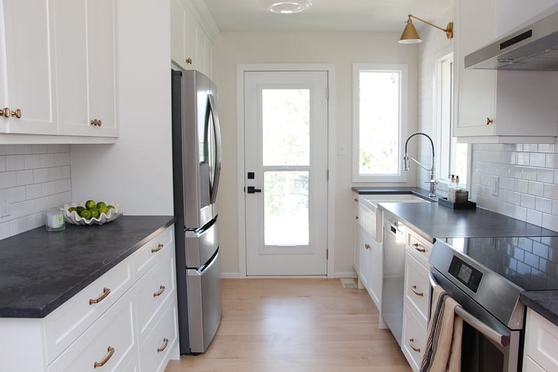 white galley kitchen with black quartz countertop, farmhouse sink, gold hardware