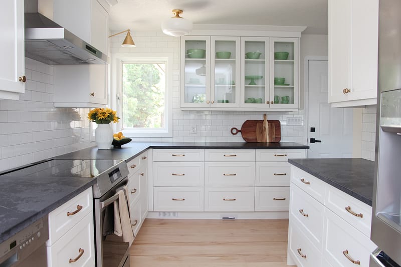 timeless white kitchen cabinets, black quartz counter, gold sconce over window, sunflowers and lemon decor, subway tile to ceiling, glass cabinets, jadeite collection