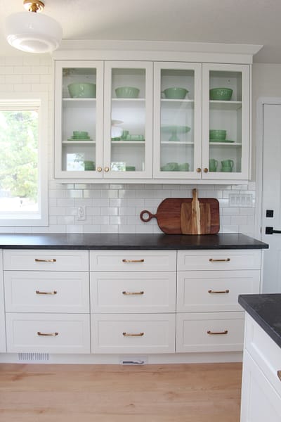 timeless white kitchen cabinets, black quartz counter, gold sconce over window, sunflowers and lemon decor, subway tile to ceiling, glass cabinets, jadeite collection