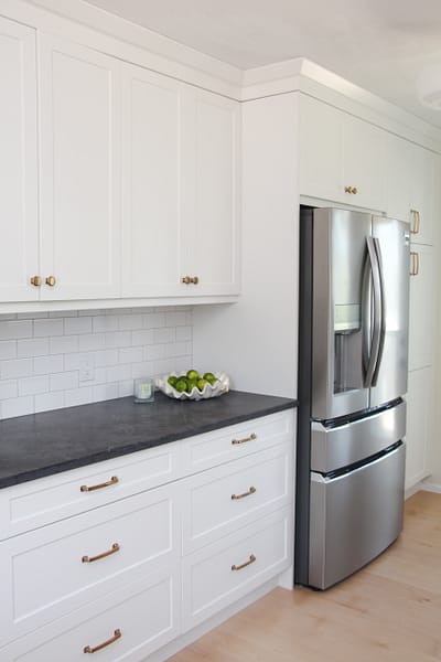 white galley kitchen with black quartz countertop, bowl of limes, gold hardware