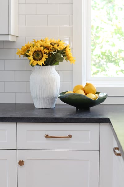 timeless white kitchen cabinets, black quartz counter, gold hardware, sunflowers and lemon decor, subway tile to ceiling